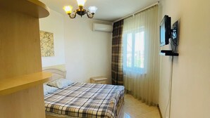 Een slaapkamer met een bed, een aan de muur bevestigde televisie, een raam met gordijnen, een airconditioning en een trap.