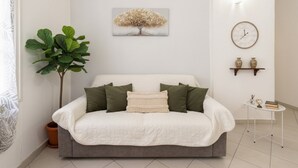 Un dormitorio con una cama, una planta verde grande, un reloj de pared y una estantería con dos jarrones.