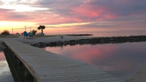 Une jetée en bois s’étendant sur des eaux calmes, avec un coucher de soleil en arrière-plan.