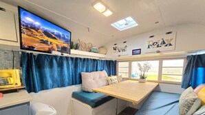 Un intérieur de camping-car compact comprenant un téléviseur, un coin salon et une petite table.