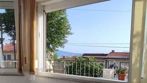 Ein Zimmer mit großem Fenster, Meerblick und einem Balkon mit Geländer.