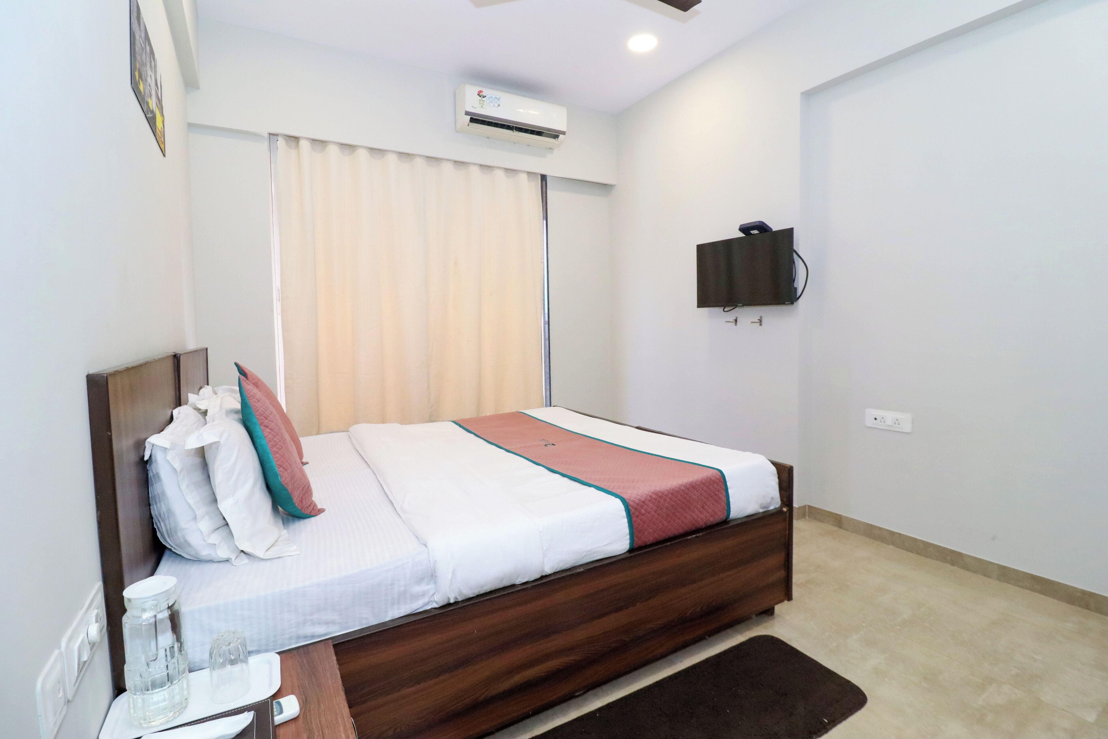 Een keurig opgeruimde hotelkamer met een bed, nachtkastje en een airconditioner.