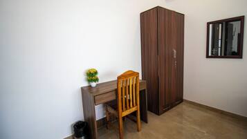 Una habitación con un escritorio de madera, una silla, un armario, un bote de basura y una pequeña planta en maceta.