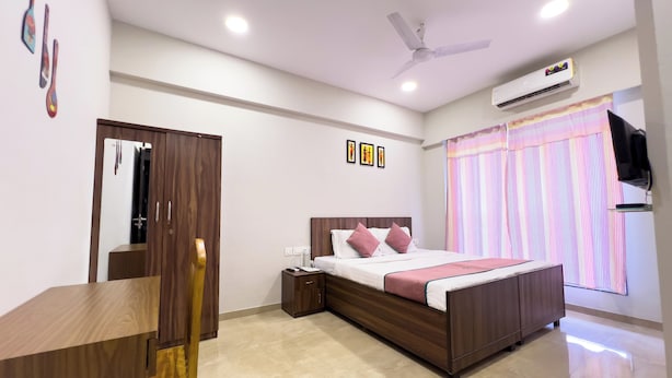 Une chambre moderne comprenant un lit, une table de chevet, une armoire, un ventilateur de plafond, un appareil de climatisation et une fenêtre avec des rideaux.