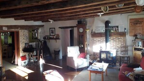 A rustic living room with a fireplace, a sofa, a dining table, and a guitar. - Old renovated house in the heart of the Parc des Écrins for nature lovers (Champoléon)