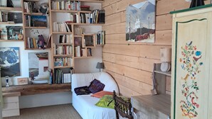 A cozy room with a white sofa, wooden bookshelves, a small desk, and a decorative cabinet. - Old renovated house in the heart of the Parc des Écrins for nature lovers (Champoléon)