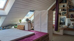 A loft bedroom with a sloped ceiling, a skylight, a bed with a purple bedspread, a globe, and a bookshelf with books and decorative items. - Old renovated house in the heart of the Parc des Écrins for nature lovers (Champoléon)