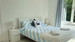 Een slaapkamer met een bed, nachtkastjes, een lamp, een vloerkleed en een raam met gordijnen.