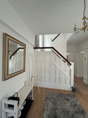 A staircase with white paneling, a wooden handrail, and a chandelier.