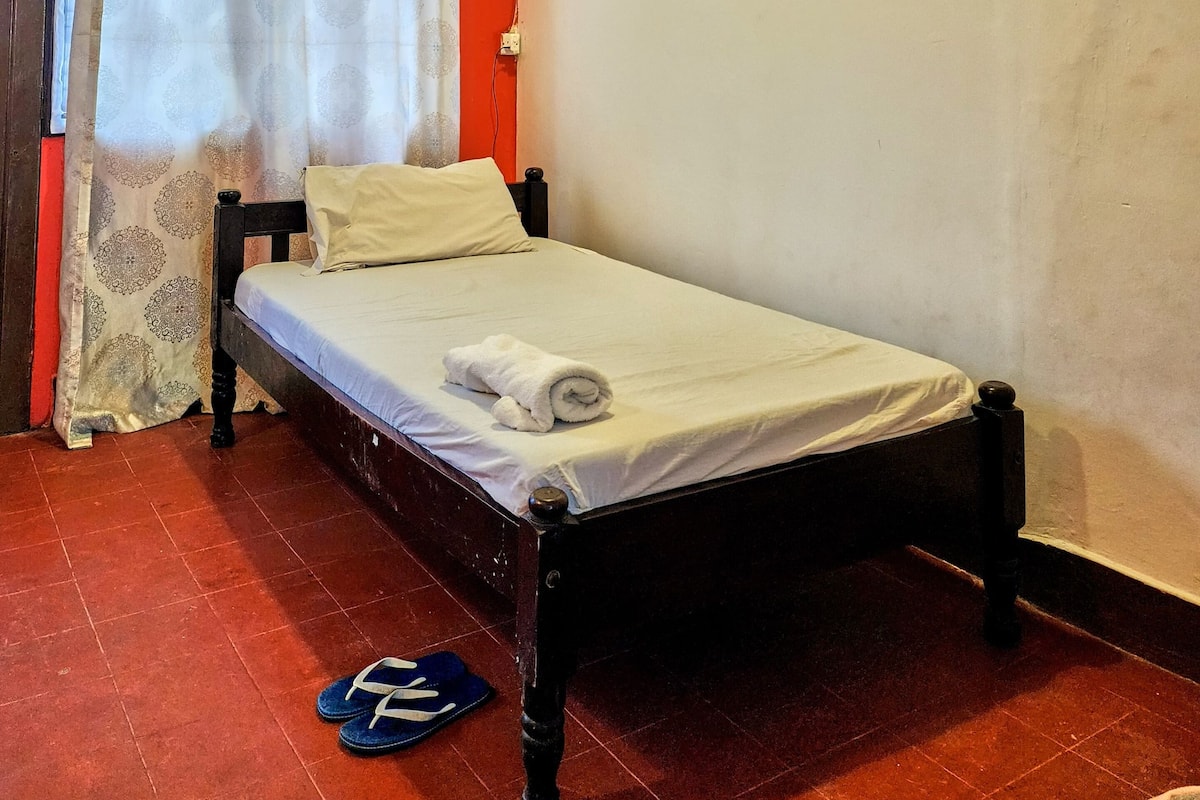Una cama individual con colchón y almohadas blancos, cabecera de madera y pared roja.