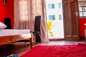 Un dormitorio con cama, una silla, un tapete rojo y vistas a un edificio a través de una puerta.
