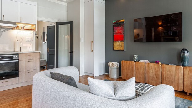 A modern living room with a grey sofa, wooden sideboard, and a flat-screen TV mounted on the wall.