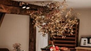 Een houten tafel met een vaas gedroogde bloemen, een fruitschaal en een mand met boeken.