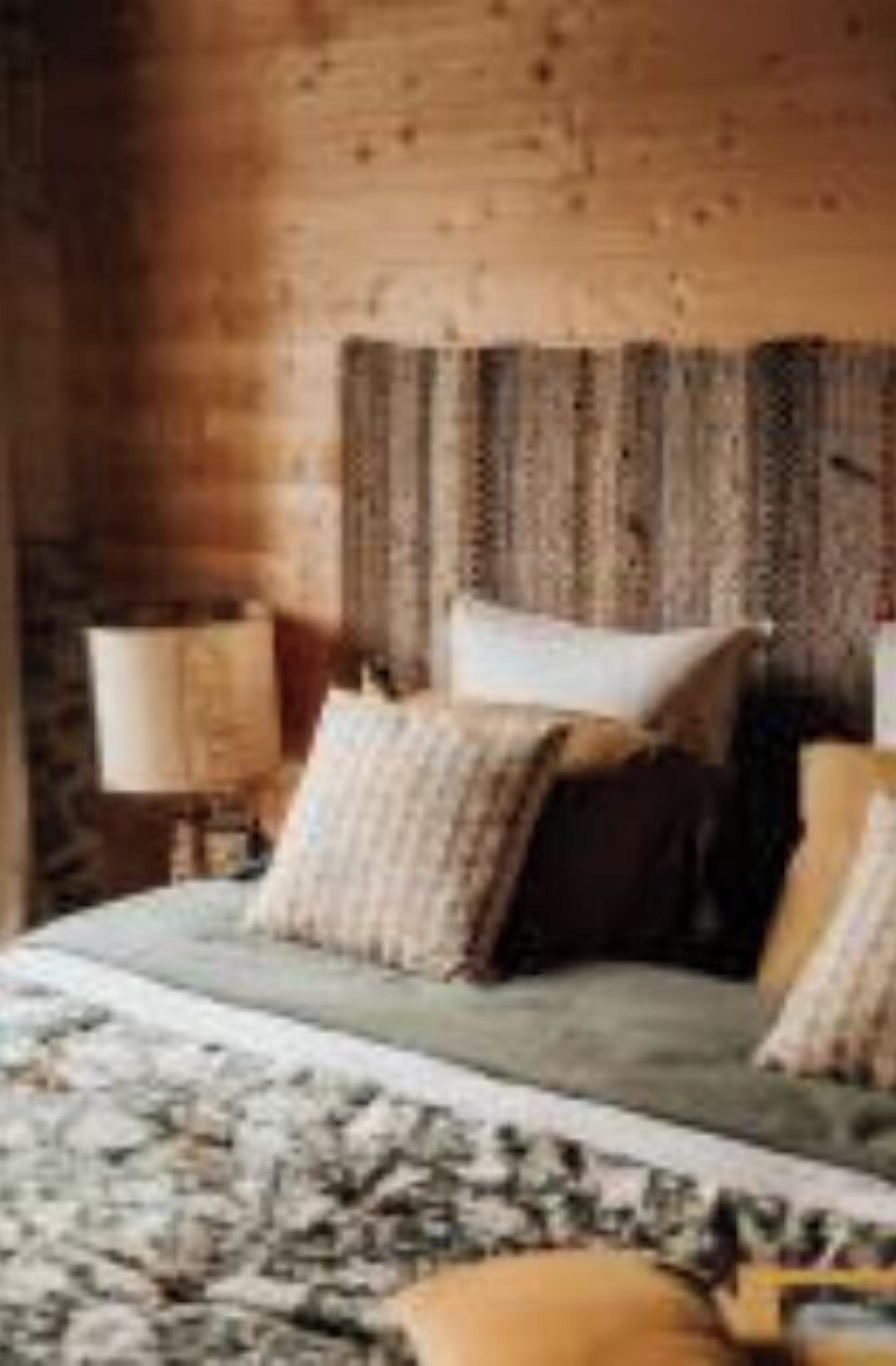Une chambre de style cabane en bois, avec un lit, des oreillers et une table de chevet dotée d’une lampe.
