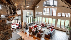 A spacious loft-style living area with high ceilings, large windows, and a rustic stone wall. - The Elmwood Wellness Estate (Dundas)