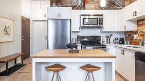 Une cuisine moderne avec des meubles blancs, des appareils en acier inoxydable et un îlot central en bois doté de tabourets.