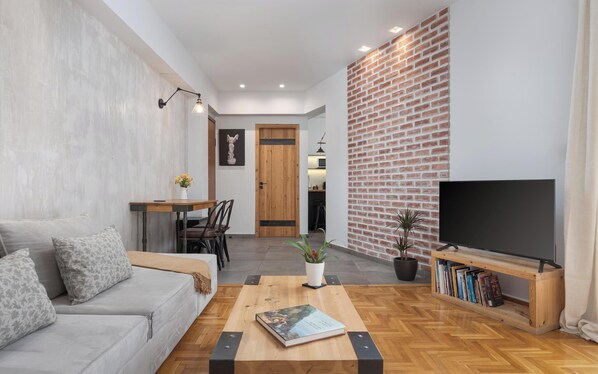 A modern living room with a sofa, coffee table, TV, and a brick accent wall.