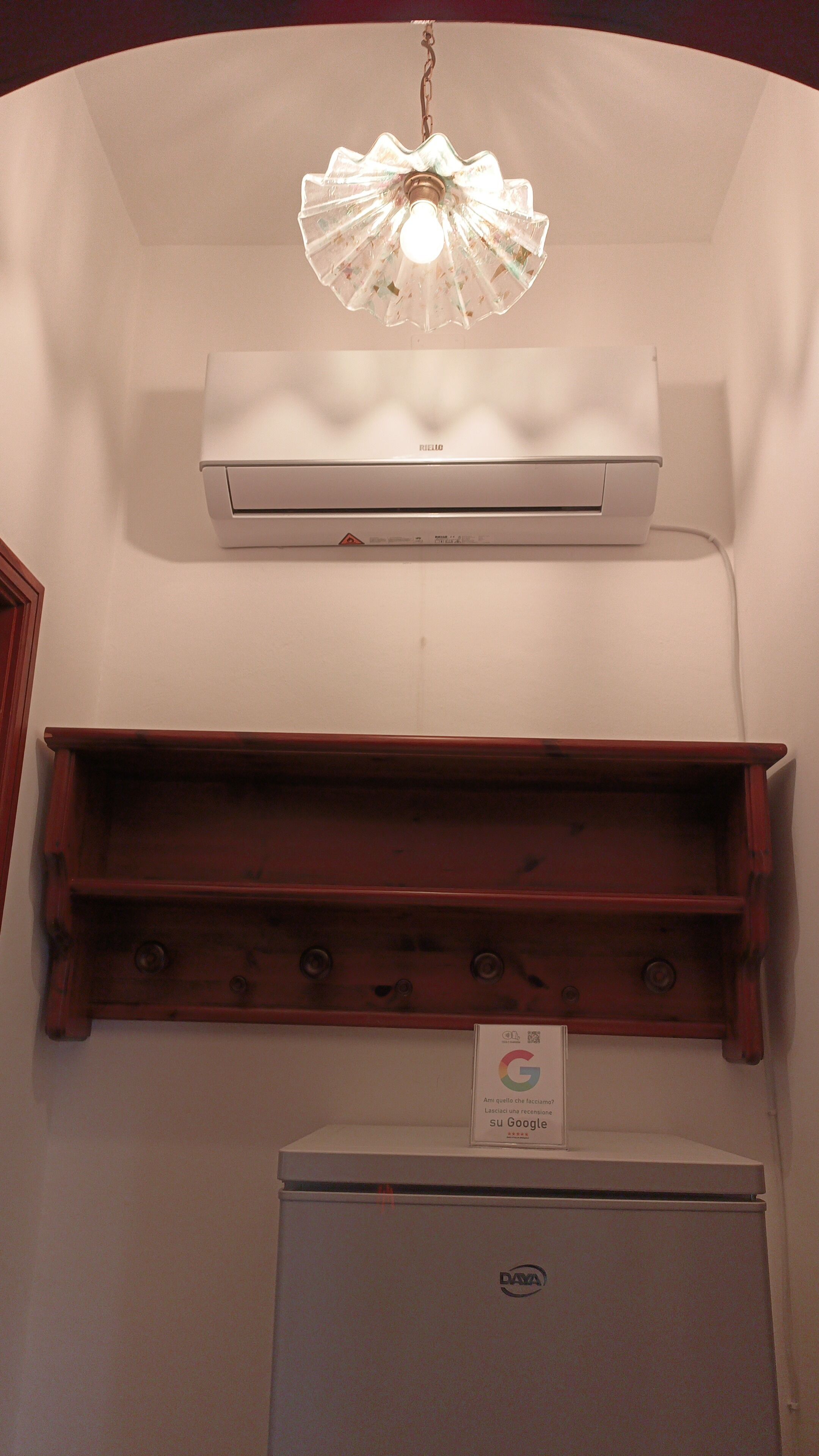 A room with a ceiling-mounted air conditioner, a wooden shelf, a refrigerator, and a sign with the Google logo.