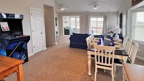 A spacious living area with a dining table set for four, a blue sofa, and a gaming console. - Ocean Heir -The Water is Calling (North Topsail Beach)
