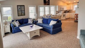 A living room with a sectional sofa, a coffee table, and a dining area with a table and chairs. - Ocean Heir -The Water is Calling (North Topsail Beach)