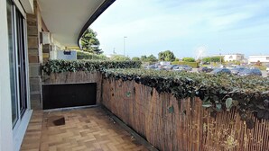 Un balcón techado con piso de baldosas, cerca de madera y vista a un estacionamiento y edificios.