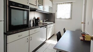 Una cocina compacta con armarios blancos, horno integrado y una mesa de comedor con sillas.