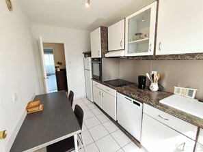 A compact kitchen with white cabinets, a black countertop, and a dining area with a table and chairs.