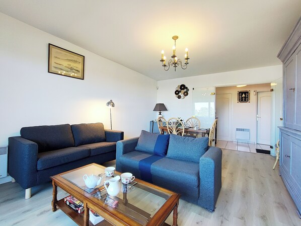 A living room with a sofa, a coffee table, and a dining area with chairs and a table.