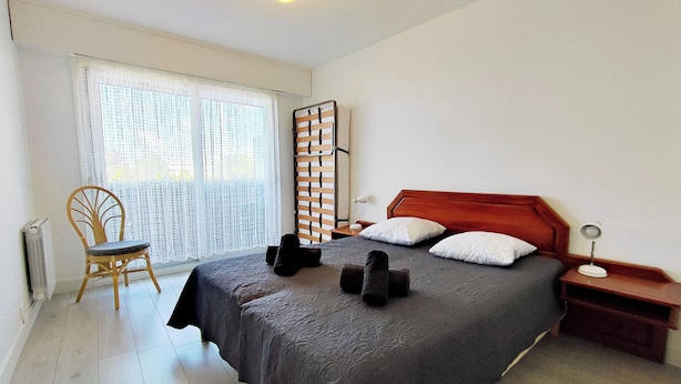 Un dormitorio con una cama grande, una silla, una mesita de noche y una ventana con cortinas.