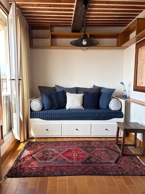 Um quarto aconchegante com um sofá azul, um tapete estampado e teto de madeira.