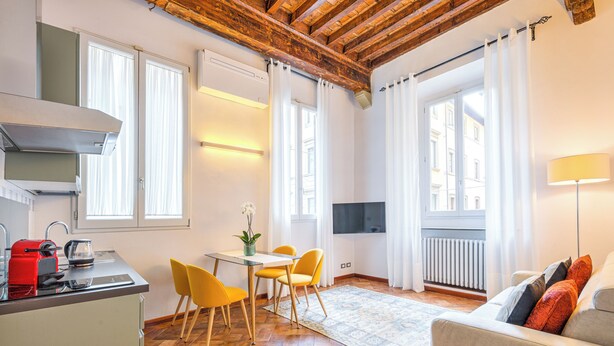 Une cuisine moderne avec une bouilloire rouge, une table à manger avec des chaises jaunes et un canapé avec des coussins orange.
