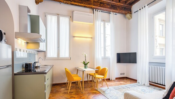 Eine kompakte Küche mit modernen Geräten, ein Essbereich mit gelben Stühlen und ein Wohnbereich mit Sofa und Fernseher.