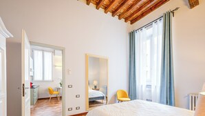 Une chambre à coucher avec un lit, un miroir, une chaise et une vue sur l’extérieur par une fenêtre.
