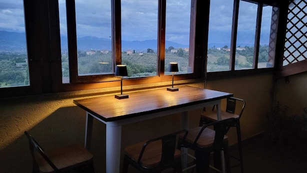 Une table avec deux chaises et deux lampes, placée près d’une fenêtre donnant sur un paysage.