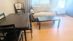 Ein Zimmer mit Esstisch, Stühlen, einer Couch und einem Fenster mit Vorhängen.