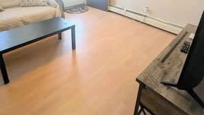 Ein Zimmer mit einer Couch, einem Couchtisch, Holzboden, Deckenventilator und einer Wand-Klimaanlage.