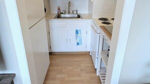 Eine kleine Küche mit weißen Schränken, einer Edelstahl-Spüle und Holzboden.