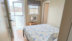 Ein Schlafzimmer mit Bett, einem Vorhangfenster, einem Deckenventilator und einer Tür, die auf einen Balkon führt.