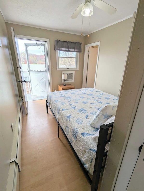 Un dormitorio con una cama, una ventana con cortinas, un ventilador de techo y una puerta que da a un balcón.