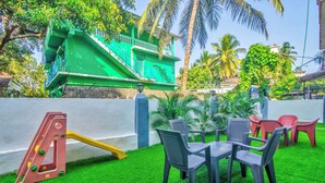 A green building with a balcony, a slide, and a table with chairs in a garden area. - Jacks Calangute place (Calangute)