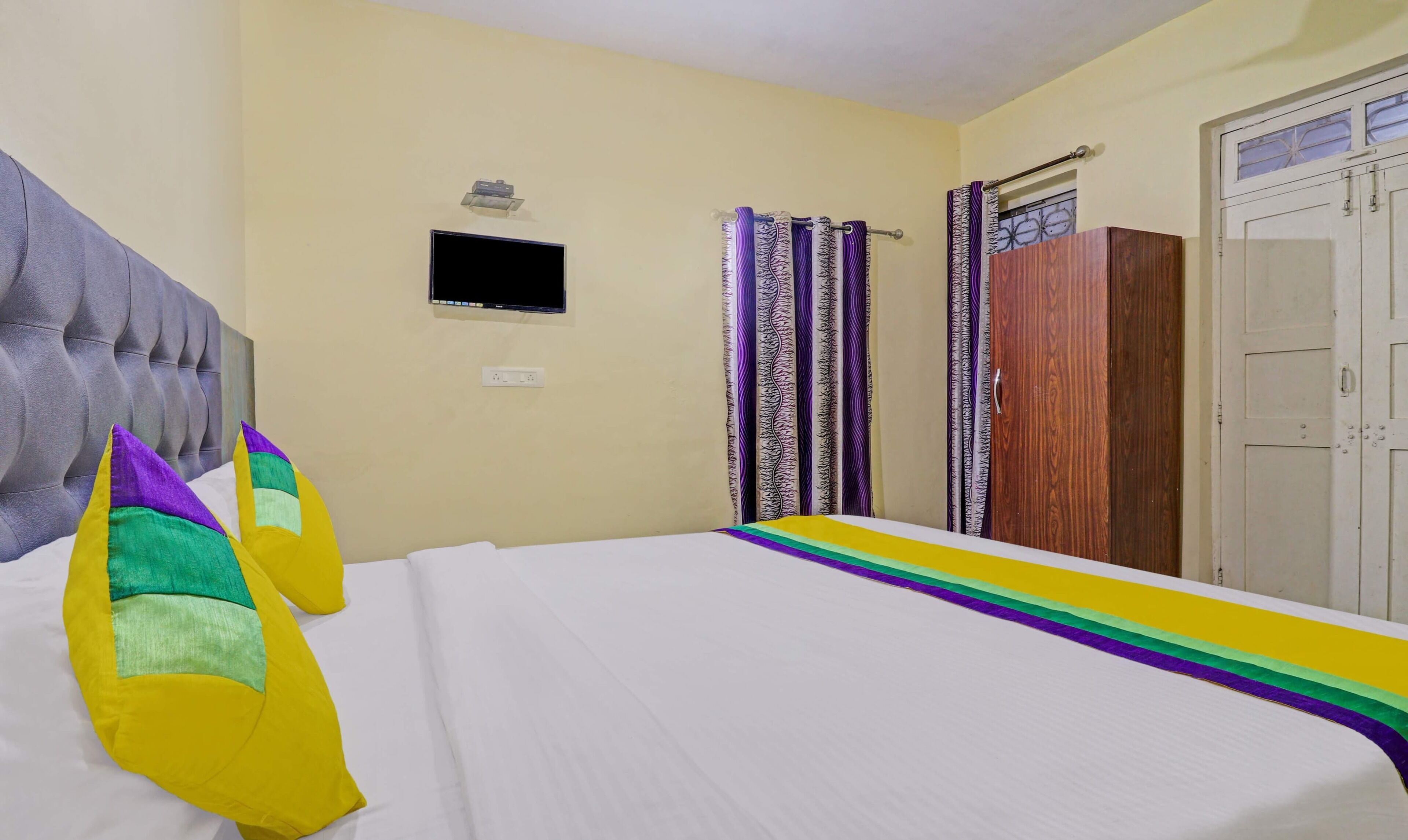 A hotel room with a bed, a television on the wall, a wardrobe, and curtains.