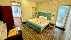 A hotel room with a green tufted bed, a wooden floor, a desk with a menu, and a view of the bathroom. - Jacks Calangute place (Calangute)