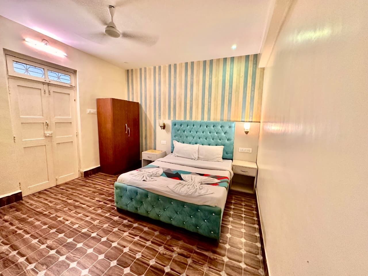 A hotel room with a bed, a wardrobe, a ceiling fan, and striped wallpaper.