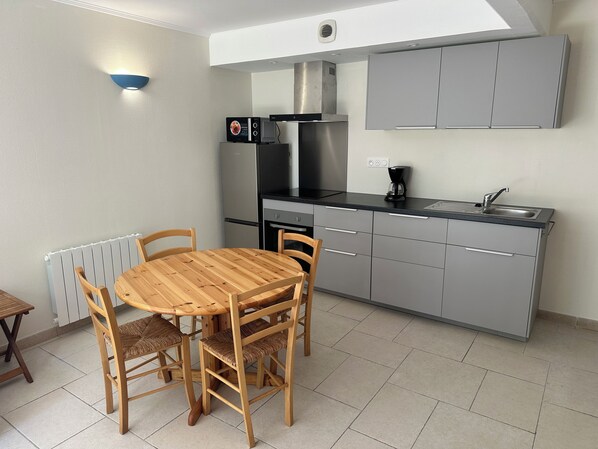 A compact kitchen with grey cabinets, a black countertop, a built-in microwave, and a coffee maker. There is a round wooden table with four chairs.