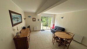 A spacious room with a wooden dining table and chairs, a sofa, a TV, and a painting on the wall.
