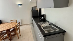 A compact kitchen with a wooden dining table, a built-in sink, and a coffee machine.