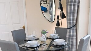 Een eettafel met vier grijze stoelen, een glazen blad en een centrale vaas met bloemen.