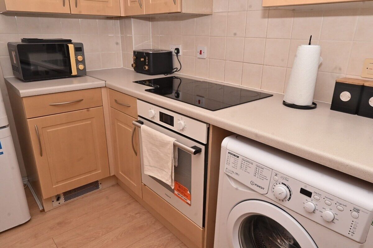 A compact kitchen with a microwave, toaster, stove, oven, and washing machine.