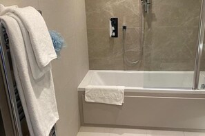 A modern bathroom with a glass-enclosed shower, a white bathtub, and a towel rack with multiple towels. - Cosy London Apartment Near River Thames (London)