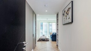 A hallway with a dark door, a light-colored herringbone floor, and a blue sofa in the background. - Cosy London Apartment Near River Thames (London)